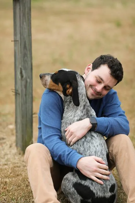 a picture of a dog walker sitting and hugging a dog